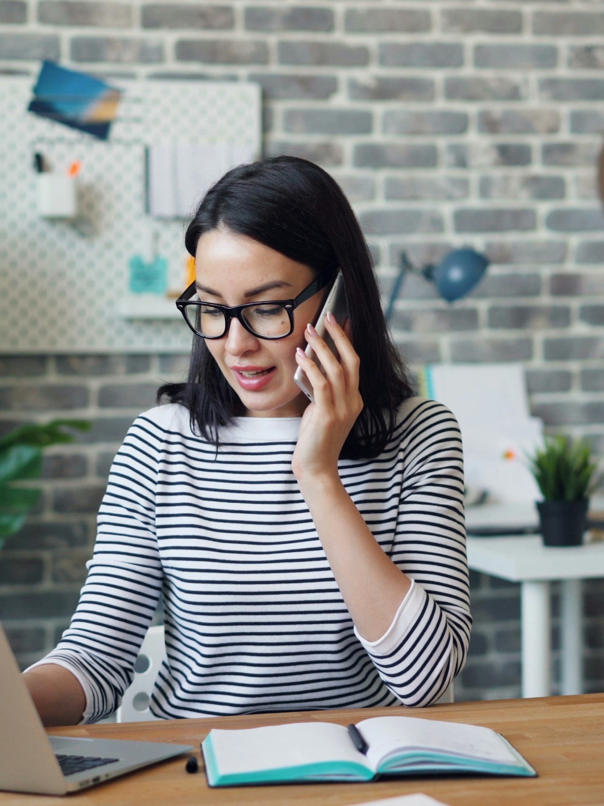 A non-profit director on the phone at her desk, laptop and notebook open